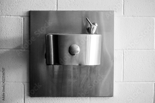 Black and white photo of water fountain attached to white washed brick wall