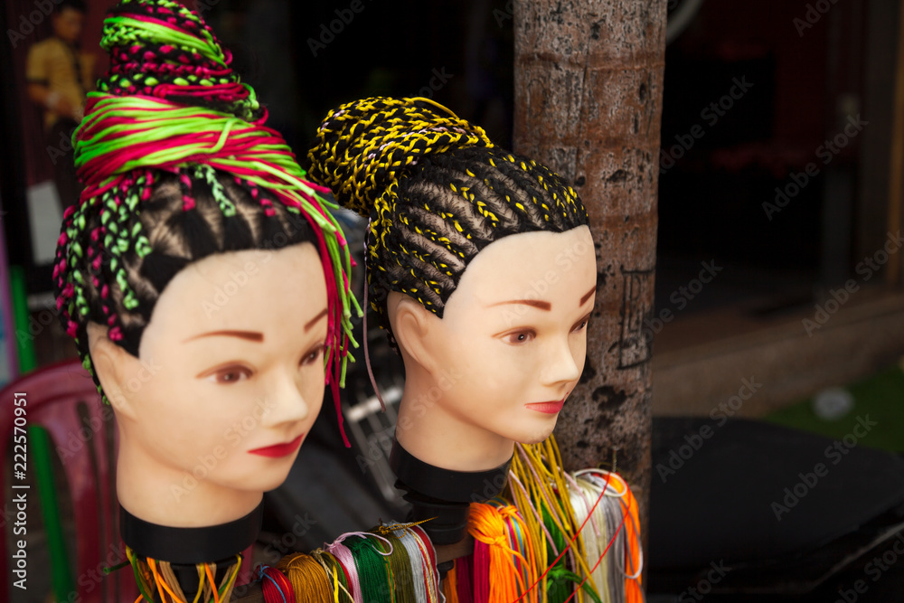 Street hairdresser salon offering braids hairstyle service. Two women heads dummies demonstrating hairdos with colorful strings