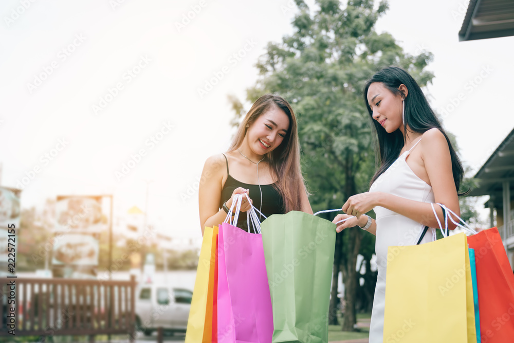 Beautiful asian female friends standing and looking in paper bag at outdoors shopping mall center retail in the city.