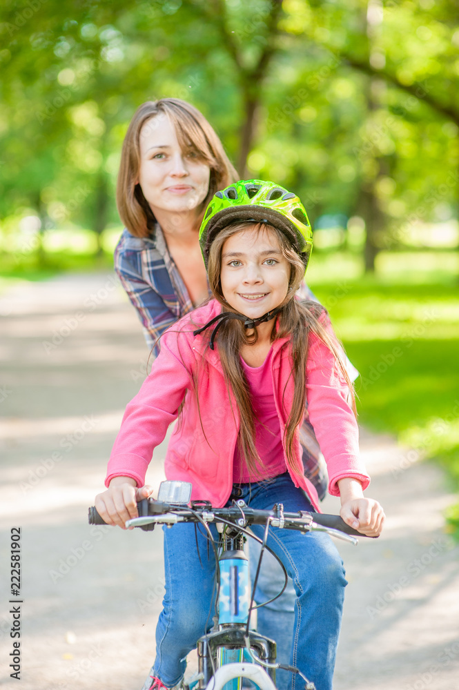 Obraz premium Smiling mother teaches her daughter to ride a bicycle in the park