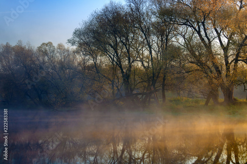 Orange sunrise over the river surface with fog in autumn morning. River landscape at sunrise