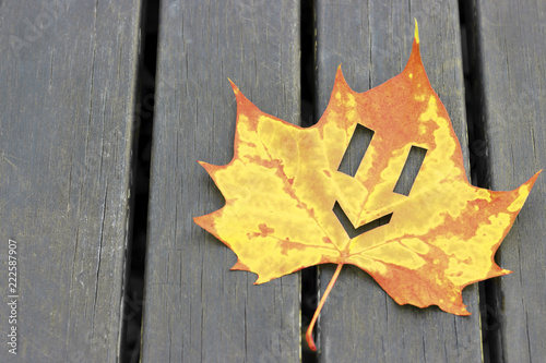 Smiley on  maple leaf on wooden background, concept of good mood, autumn background, copy space photo