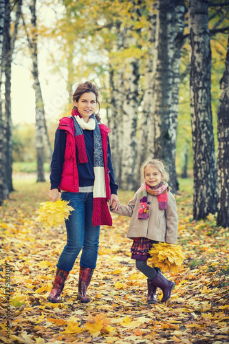 Smiling little girl and her mother enjoy walk in autumn park and play with bright autumn leaves