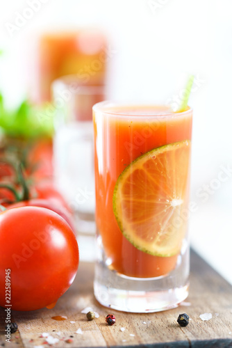 Sangrita in a shot glass served with fresh tomatoes, celery sticks and black pepper. Tequila bottle in bokeh, wooden board, high resolution.