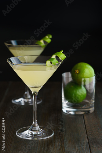 Two daiquiris served in cocktail glasses, garnished with lime zest. Dark wooden background, high resolution.