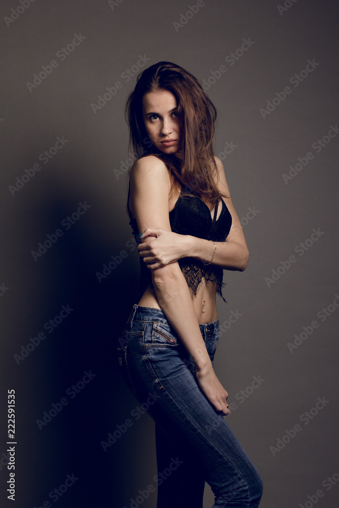 Young brunette female in black bra jeans and leather jacket over grey background
