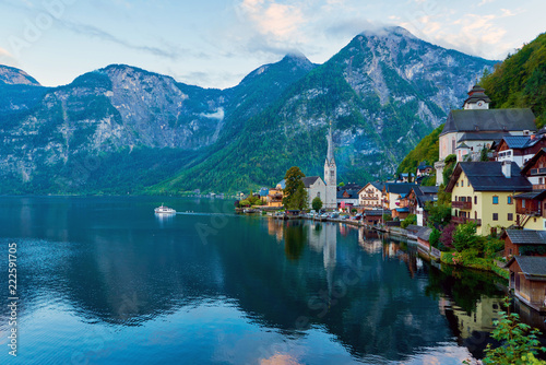 Scenic picture-postcard view of famous Hallstatt mountain village with Hallstatter lake and boat in Austrian Alps. Autumn sunset on Hallstatt lake with beautiful clouds.