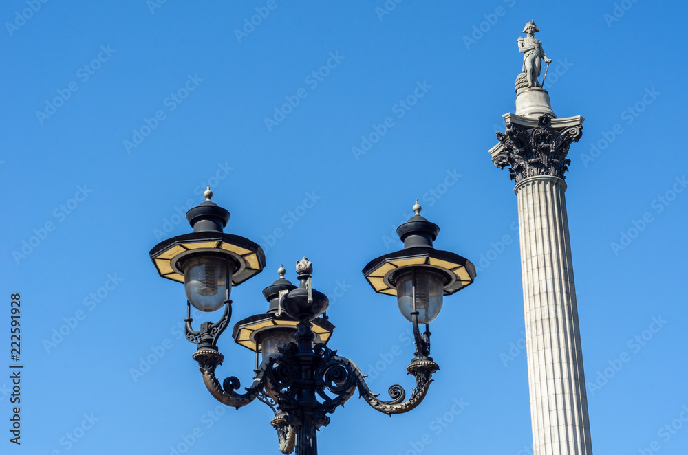 Low angle view of street lights and the iconic Nelson's Column against a clear blue sky at Trafalgar Square, London