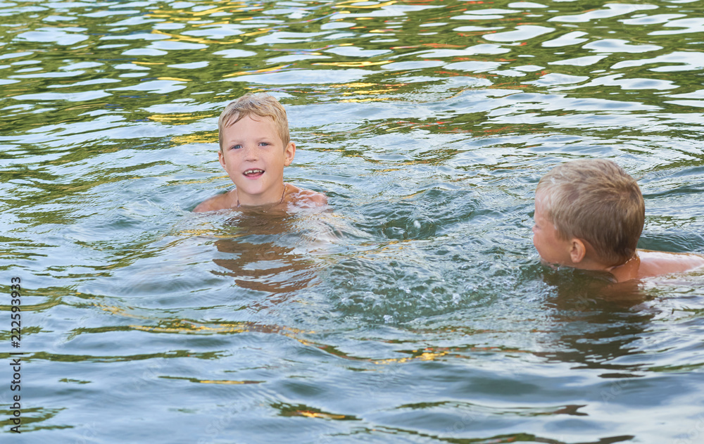 Young cute boy and his little brother playing in the water in a beautiful river or lake on a sunny summer day