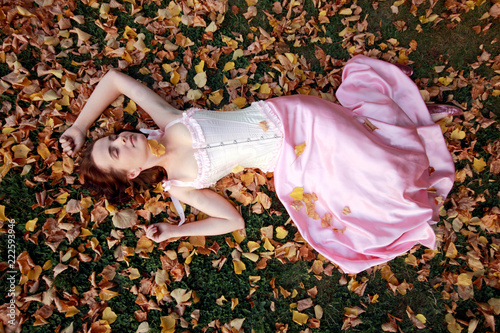 Fine emotional brunette sleep on autumn leaves and grass, top view. Yonge girl in vintage pink pastel with live expressions on beautiful country and old background.