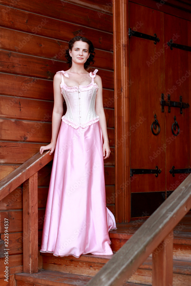 Fototapeta premium Fine emotional brunette on old style veranda, full length. Yonge girl in vintage pink pastel with live expressions on beautiful country and old background.