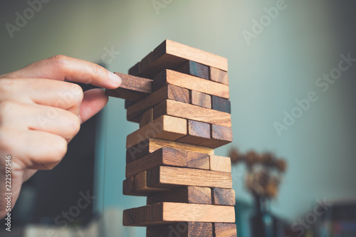 Closeup image of a hand holding and playing Jenga or Tumble tower wooden block game