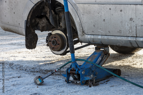 Mounting in winter. The car was lifted on the jack and the wheel was removed. The pneumatic wrench is located on the asphalt covered with snow.