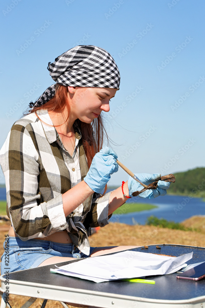 Beautiful girl archaeologist carefully clears the find with a brush