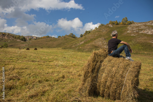 a man resting after work on a haystack in a field with a harvested crop