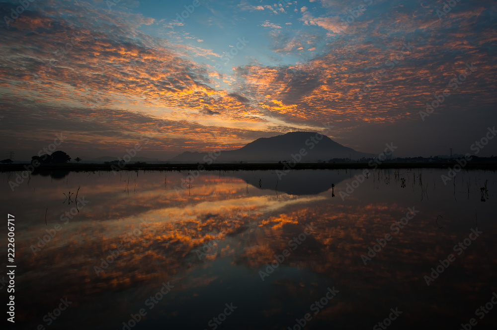 Fototapeta premium Dramatic sunrise with beautiful cloud over a hill with reflection in the foreground