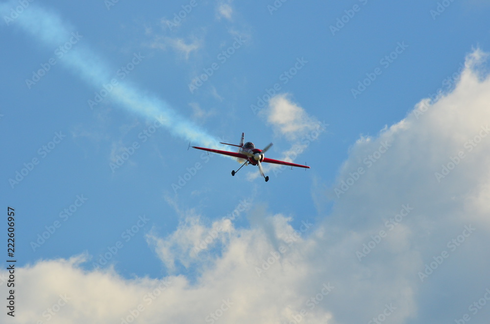 Stunt monoplane flying on cloudy blue sky leaving white smoke trail Stunt monoplane flying on cloudy blue sky leaving white smoke trail