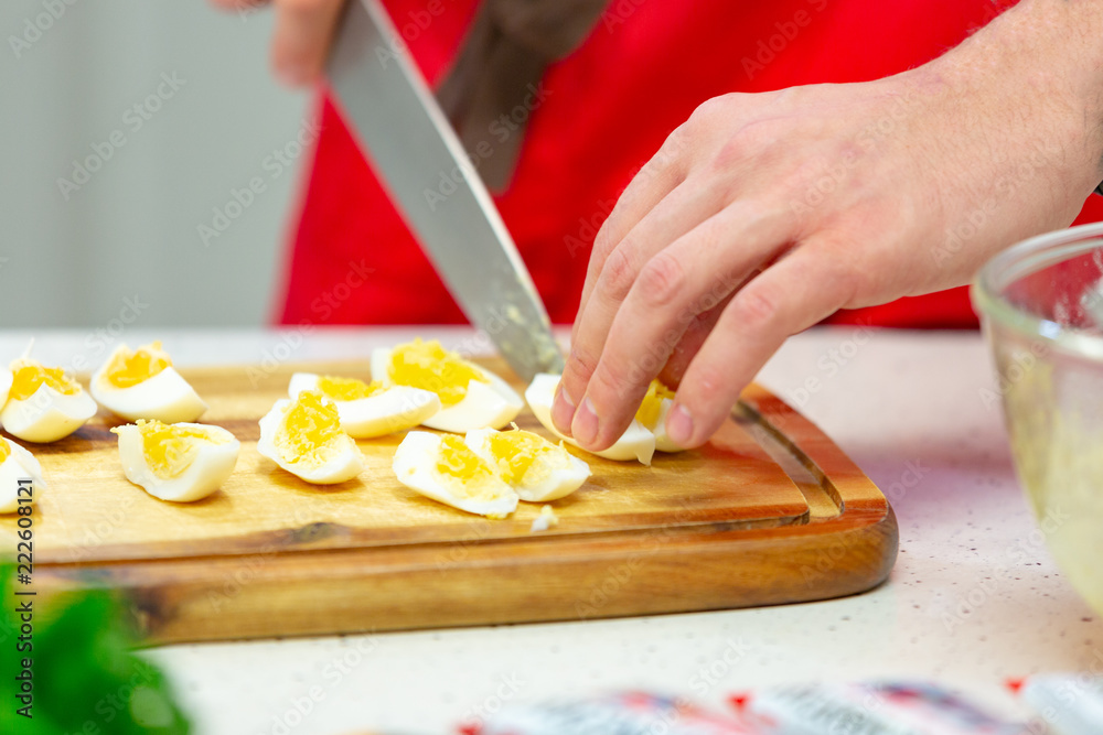 Man cuts boiled quail eggs on wooden cutting board close-up. Step by step recipe of homemade tuna salad. Man cuts boiled quail eggs on wooden cutting board close-up. Step by step recipe of homemade tuna salad.