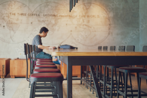 Vacancy chairs and wooden table with blurred unidentified man working with his laptop in background at the coffee shop. photo