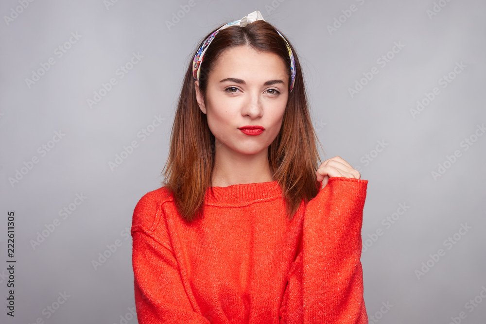 Cheerful lovely female has pleasant smile, being in high spirit, rejoices meeting with friends, dressed in fashionable red oversized sweater and bandana, poses on gray background. Show what you got. Cheerful lovely female has pleasant smile, being in high spirit, rejoices meeting with friends, dressed in fashionable red oversized sweater and bandana, poses on gray background. Show what you got.