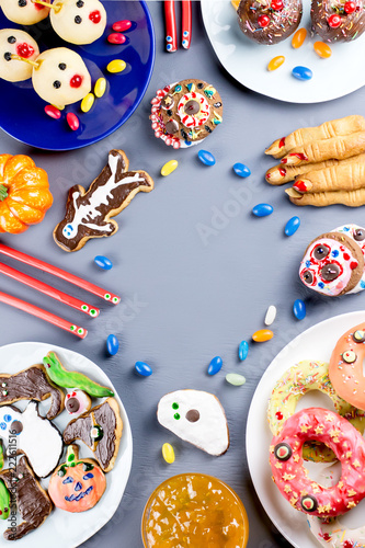 Halloween sweet treats, party food concept. Scary cookies, monster biscuits and fruits on grey background.