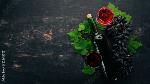 Red wine in a bottle with a glass and grapes. On a black wooden background. Free space for text. Top view.