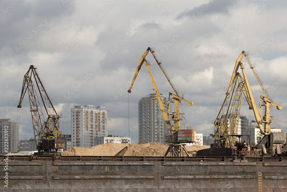 A barge in the river port and working cranes on the city background