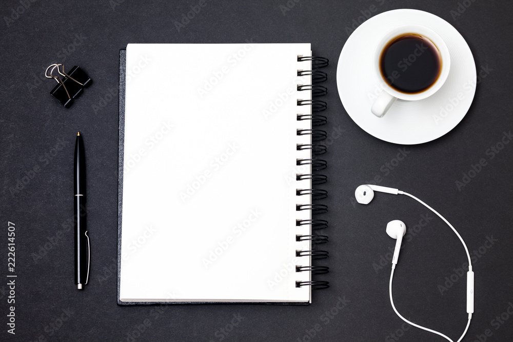 Business flat lay composition: minimal workplace with blank notepad, pencil, coffee cup, headphones and supplies on black table. Top view. Businessman or student desk. Business flat lay composition: minimal workplace with blank notepad, pencil, coffee cup, headphones and supplies on black table. Top view. Businessman or student desk.