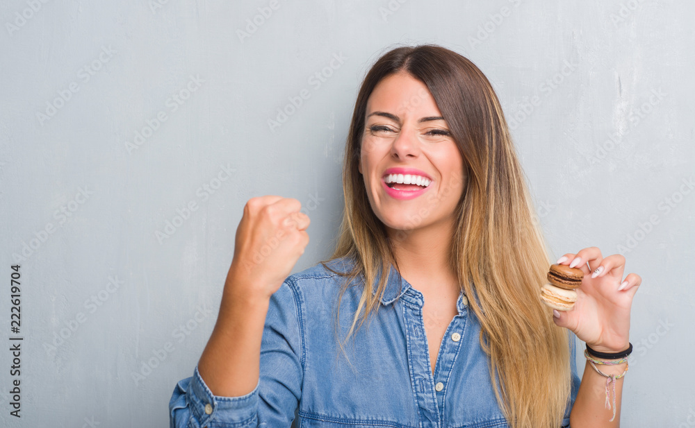 Young adult woman over grey grunge wall eating chocolate macarons annoyed and frustrated shouting with anger, crazy and yelling with raised hand, anger concept Young adult woman over grey grunge wall eating chocolate macarons annoyed and frustrated shouting with anger, crazy and yelling with raised hand, anger concept