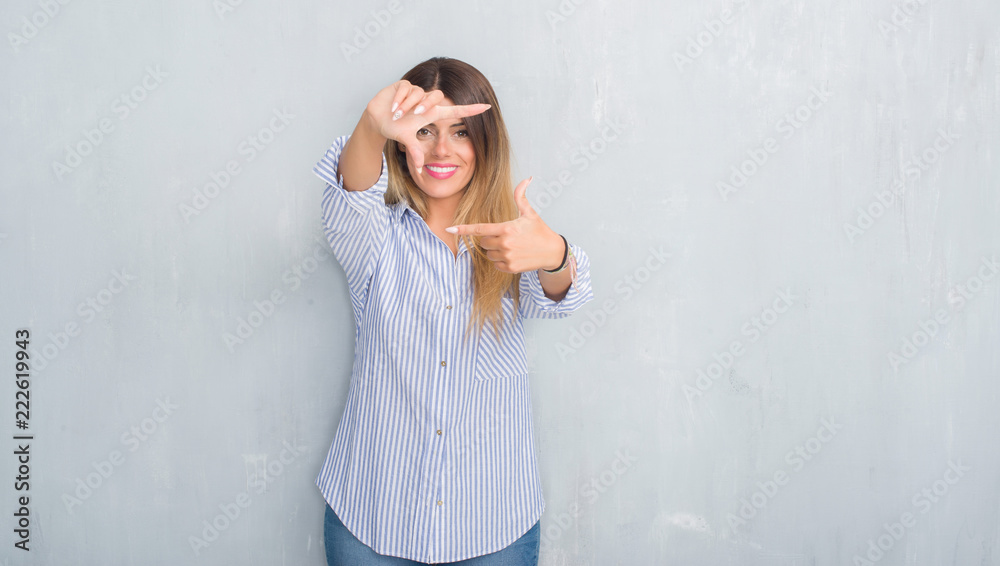 Young adult woman over grey grunge wall wearing fashion business outfit smiling making frame with hands and fingers with happy face. Creativity and photography concept. Young adult woman over grey grunge wall wearing fashion business outfit smiling making frame with hands and fingers with happy face. Creativity and photography concept.