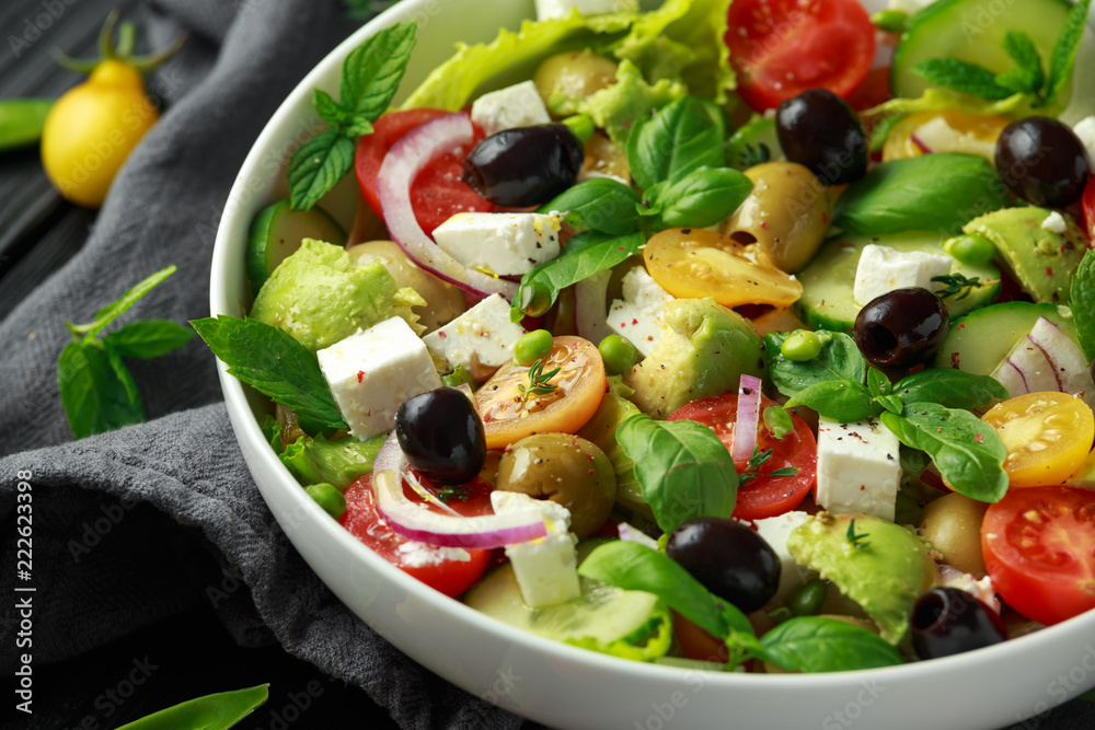 Healthy low calories salad with lettuce, heirloom tomatoes, avocado, feta cheese, red onion, cucumber, sweet peas, olives, thyme, mint and basil.