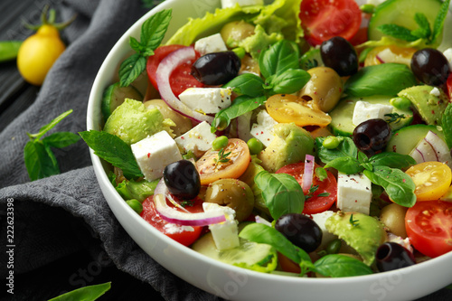 Healthy low calories salad with lettuce, heirloom tomatoes, avocado, feta cheese, red onion, cucumber, sweet peas, olives, thyme, mint and basil.