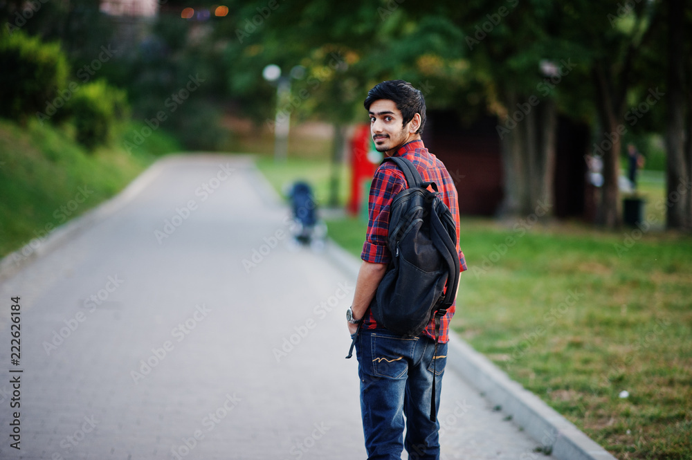 Young indian student man at red checkered shirt and jeans with backpack posed at street. Young indian student man at red checkered shirt and jeans with backpack posed at street.