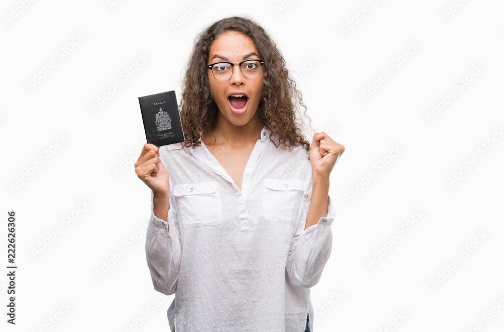 Young hispanic woman holding passport of Canada screaming proud and celebrating victory and success very excited, cheering emotion