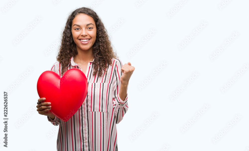 Young hispanic woman in love holding red heart screaming proud and celebrating victory and success very excited, cheering emotion Young hispanic woman in love holding red heart screaming proud and celebrating victory and success very excited, cheering emotion