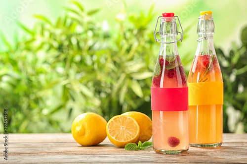 Bottles with natural lemonade on table against blurred background