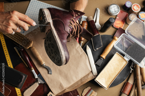 Enjoying process of creation custom made shoes. Workplace of shoe designer. Hands of shoemaker dealing with cobbler tool, close up