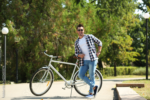 Handsome young hipster man with bicycle in park