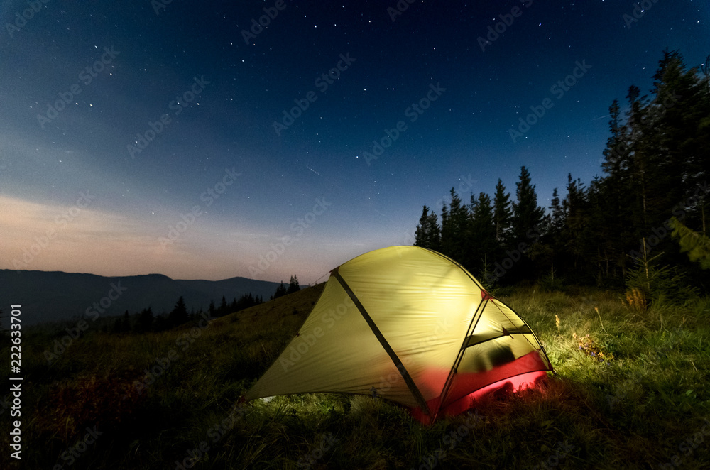 Astrophotography of night camp and starry skies at Carpatian mountains in Ukraine. Green tent on the foreground is highlighted from the inside. Concept of  backpacking travel lifestyle.