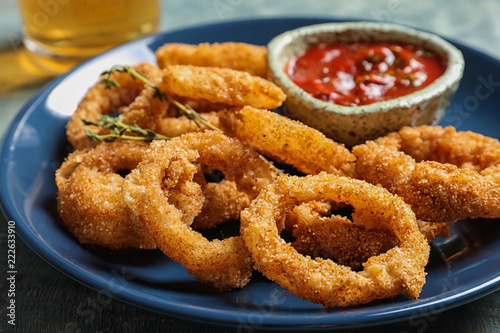 Homemade crunchy fried onion rings and tomato sauce on plate, closeup