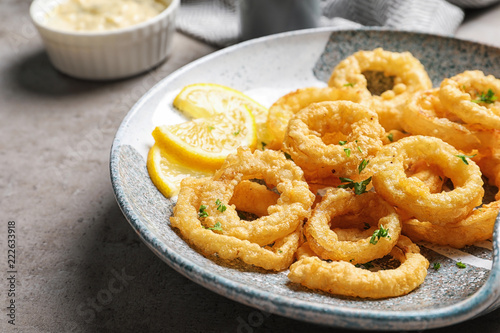 Plate with homemade crunchy fried onion rings and lemon slices on table, closeup
