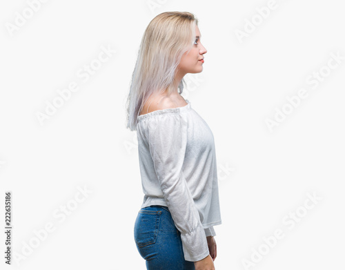 Young blonde woman over isolated background looking to side, relax profile pose with natural face with confident smile.