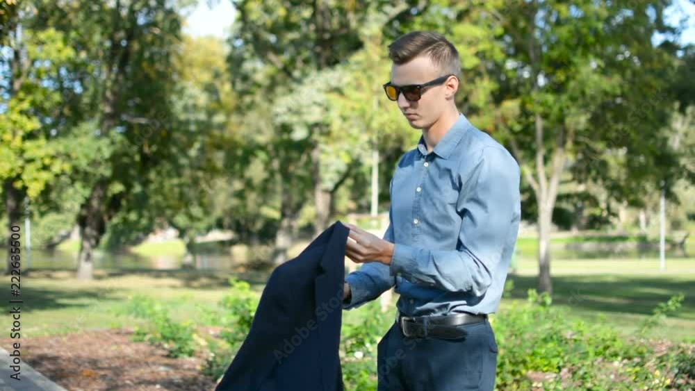 Young businessman outside in the park using mobile phone smartphone, putting suit jacket blazer and walking away Young businessman outside in the park using mobile phone smartphone, putting suit jacket blazer and walking away