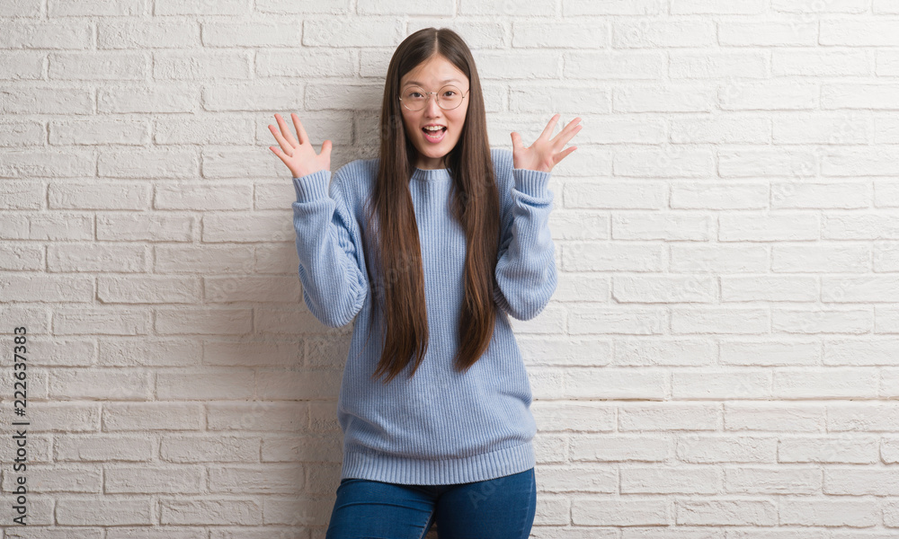 Young Chinise woman over white brick wall celebrating crazy and amazed for success with arms raised and open eyes screaming excited. Winner concept Young Chinise woman over white brick wall celebrating crazy and amazed for success with arms raised and open eyes screaming excited. Winner concept