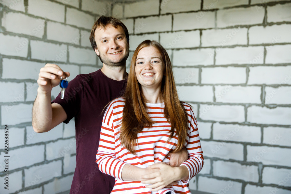 Young smiling couple showing keys to new home hugging looking at camera