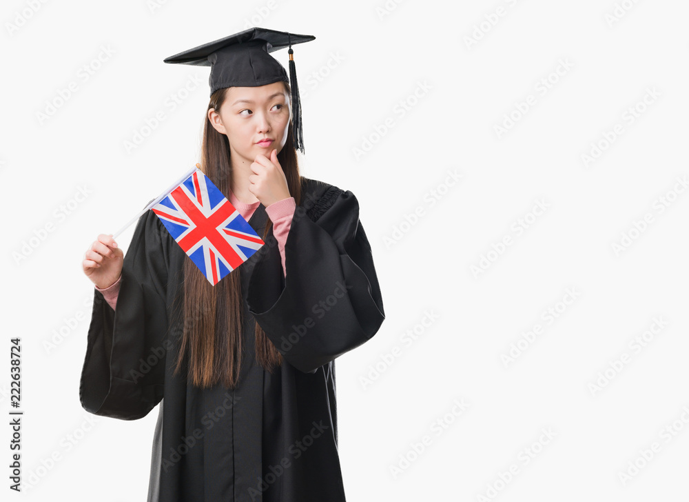 Young Chinese woman wearing graduate uniform holding United kingdom flag serious face thinking about question, very confused idea Young Chinese woman wearing graduate uniform holding United kingdom flag serious face thinking about question, very confused idea
