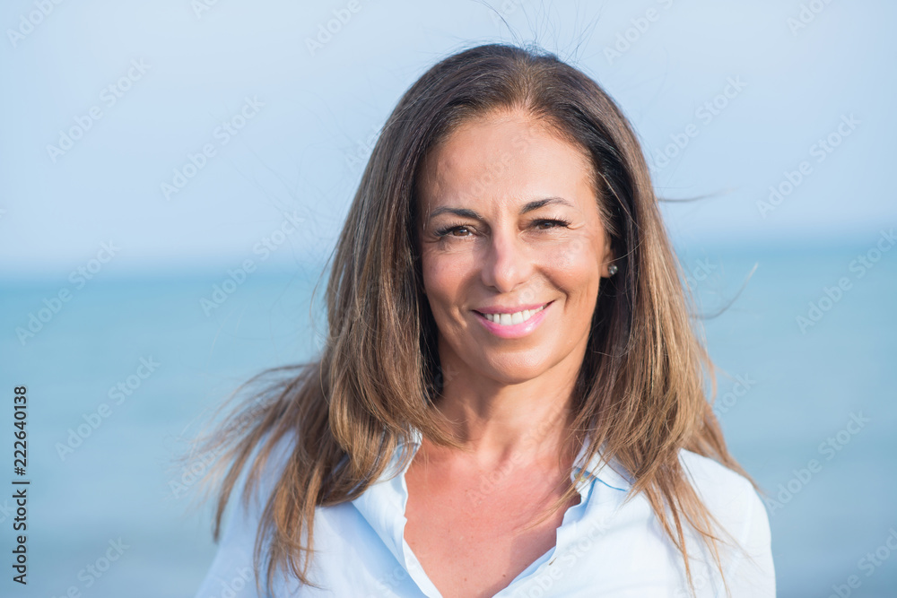 Fototapeta premium Beautiful middle age hispanic woman standing with smile on face at the ocean. Smiling confident and cheerful on a sunny day with sea view. .
