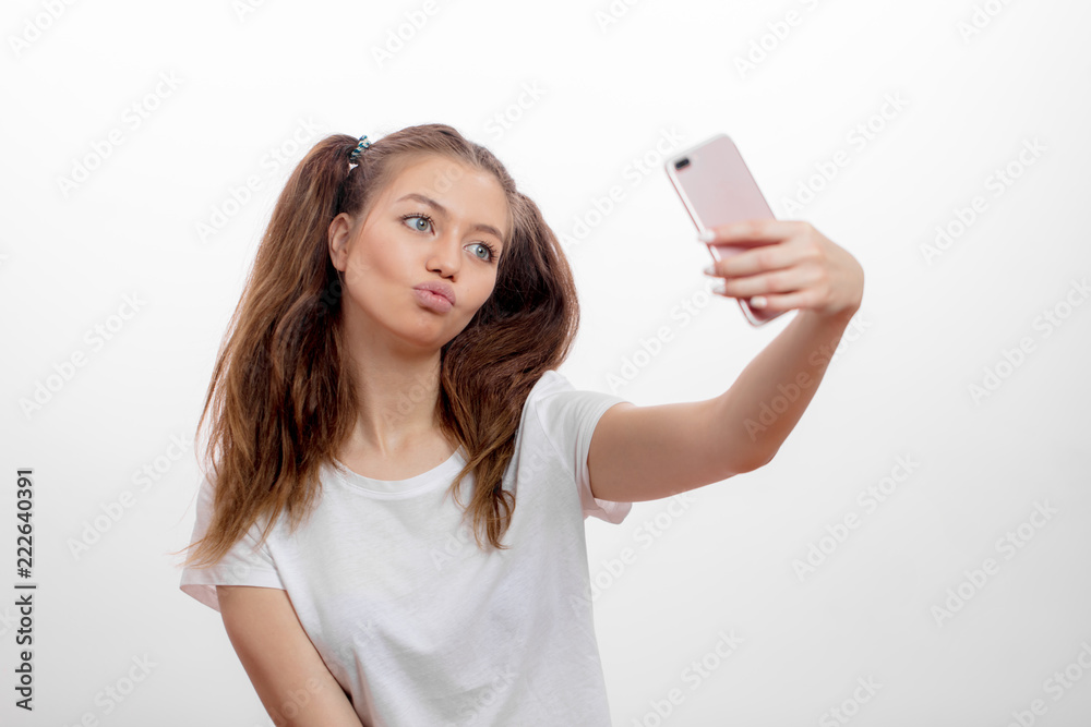 lovely awesome girl blowing kiss while taking a picture. student girl kissing to the camera, hipster with full lips looking at the screen of the smart phone