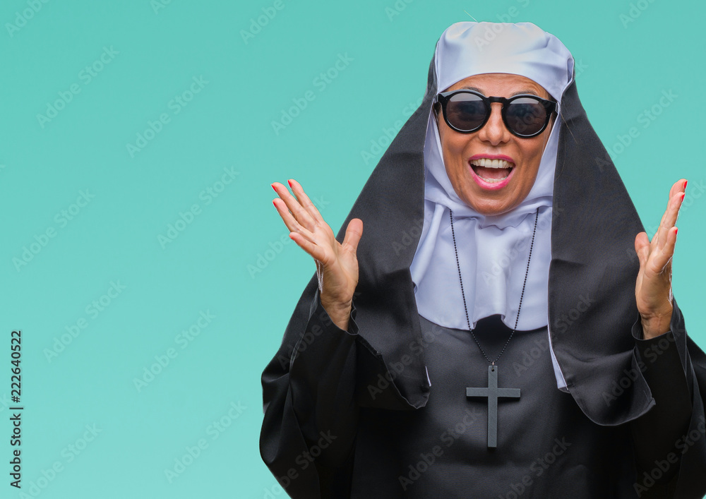 Middle age senior catholic nun woman wearing sunglasses over isolated background celebrating crazy and amazed for success with arms raised and open eyes screaming excited. Winner concept Middle age senior catholic nun woman wearing sunglasses over isolated background celebrating crazy and amazed for success with arms raised and open eyes screaming excited. Winner concept