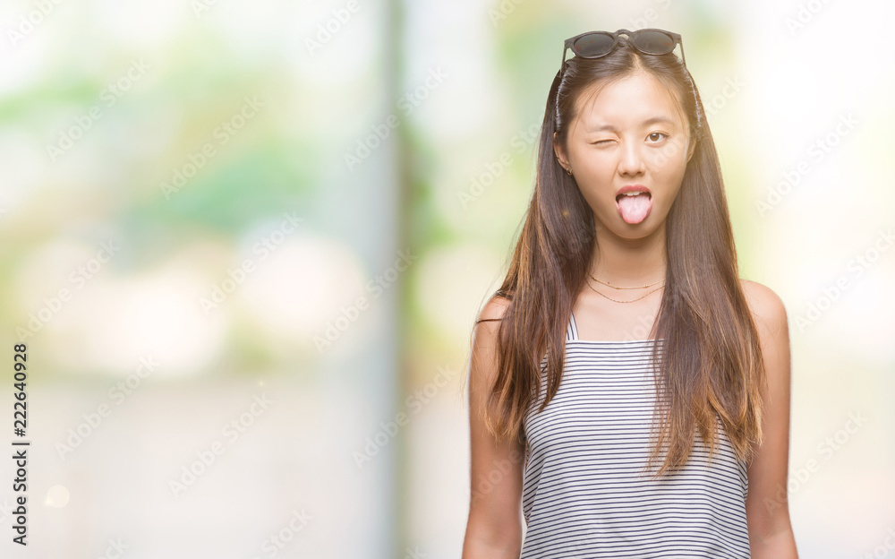 Young asian woman wearing sunglasses over isolated background sticking tongue out happy with funny expression. Emotion concept. Young asian woman wearing sunglasses over isolated background sticking tongue out happy with funny expression. Emotion concept.